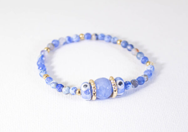 Pulsera de Protección Halo Lunar de Microcosm elegante pulsera está confeccionada con pequeñas piedras de ágata azul, ojos turcos de cerámica y detalles en chapa de oro y aluminio.
